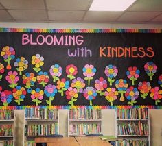 a classroom with bookshelves and flowers painted on the blackboard behind it is a sign that says blooming with kindness