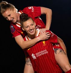 two women in red soccer uniforms are hugging each other and smiling at the camera with tattoos on their arms