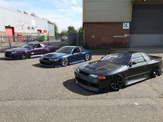 three cars parked in a parking lot next to an industrial building with garage doors open