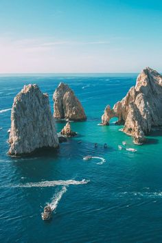 several boats are in the water near some large rocks and rock formations on the ocean