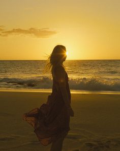 a woman standing on top of a beach next to the ocean under a sunset sky