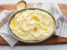 a bowl of mashed potatoes on a cutting board with a wooden spoon next to it