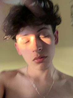 a shirtless man with his eyes closed and sun shining through the window behind him