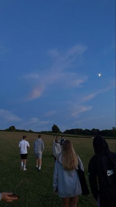 some people are flying a kite in a field at night with the moon behind them