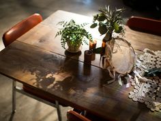 a wooden table topped with potted plants next to candles and doily on top of it