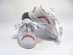 a pair of white shoes with red stitching on the laces and baseball stitches