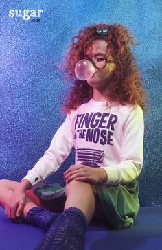 a young woman sitting on the ground blowing bubbles into her mouth while wearing glasses and socks