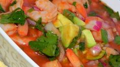 a white bowl filled with shrimp and vegetables next to crackers on a blue table cloth