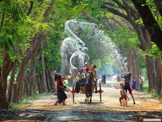 some people are riding horses and spraying water on their heads in the air as they walk down a dirt road surrounded by trees