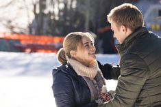 a man and woman standing next to each other in the snow smiling at each other