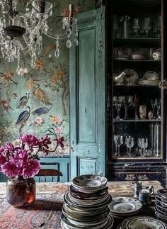 a table topped with lots of plates and vases filled with flowers next to a china cabinet