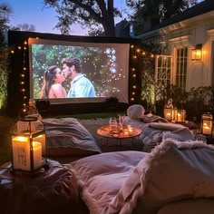 an outdoor movie is set up in front of a house with candles on the ground