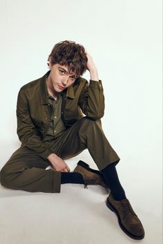 a young man sitting on the ground with his hands in his hair and wearing a green suit