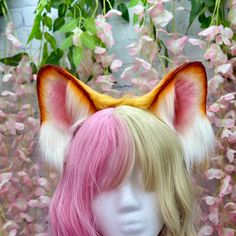 a wig with pink and yellow hair is shown in front of some flowers on display