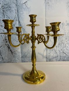 a golden candelabra with four candles on it's stand, in front of a wall