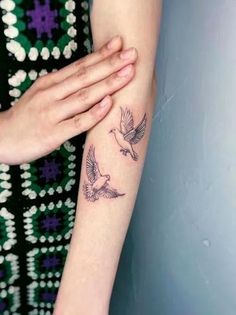 a woman's arm with two birds on it and one is holding her hand