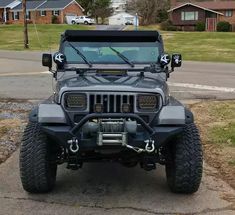 a gray jeep parked on the side of a road next to a street with houses in the background