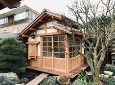 a small wooden house sitting in the middle of a garden with rocks and trees around it