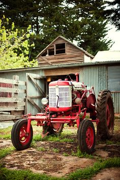 an old red tractor parked in front of a barn