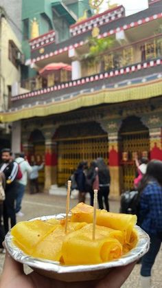 a person holding a plate with food on it in front of a building and people walking around