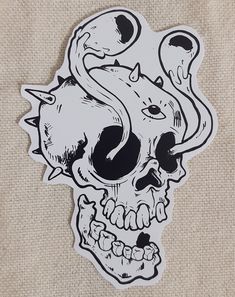 a sticker depicting a skull with horns and fangs on it's face, sitting on a piece of fabric