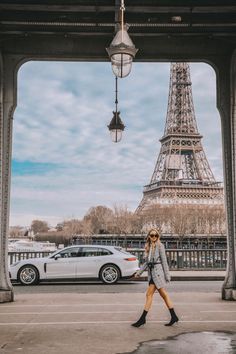 a woman is walking in front of the eiffel tower, with cars passing by