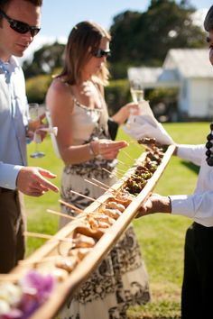 two men and one woman are serving food on skewers