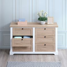 a white and wood dresser with drawers on it's sides, next to a potted plant