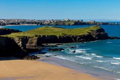 a sandy beach next to the ocean with lots of green grass on top of it