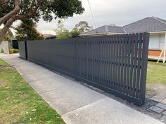 a black metal fence on the side of a sidewalk next to a tree and house