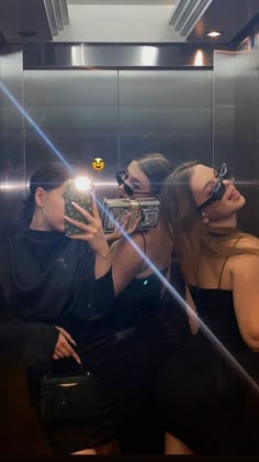 three women taking selfies in the bathroom mirror with their cell phones up to their faces