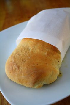 a piece of bread sitting on top of a white plate next to a paper bag