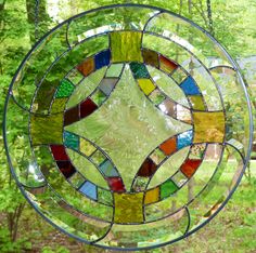 a circular stained glass window hanging from a chain in front of some trees and bushes