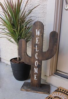 a wooden welcome sign sitting next to a potted plant on the front step of a house