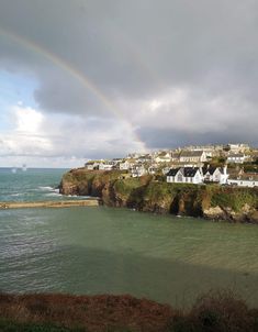 a rainbow is in the sky over some houses by the ocean and water with buildings on it