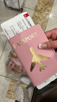 a person holding a pink passport case with gold foil on the front and an airplane sticker on the back