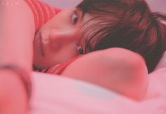 a woman laying on top of a bed next to a pink blanket and pillow with her eyes closed