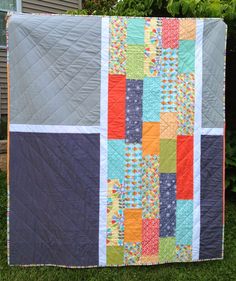 a patchwork quilt hanging on the side of a house in front of a tree