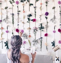 a woman sitting on a couch in front of a wall with flowers hanging from it