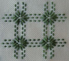 the cross is made up of small green beads on a white cloth with black stitching