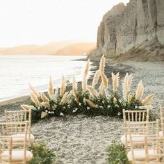 an outdoor ceremony setup with chairs, flowers and greenery on the sand by the water