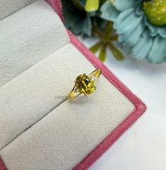 a yellow diamond ring sitting on top of a white velvet box next to blue flowers