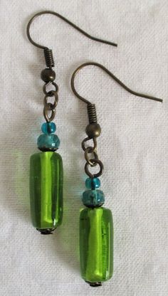 two green glass beads are hanging from silver earwires on a white cloth background