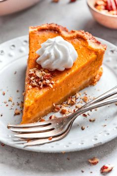 a slice of pumpkin pie on a white plate with a fork and bowl in the background