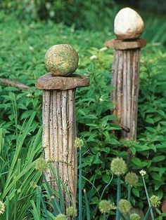 two wooden posts with balls on them are in the middle of some green plants and grass