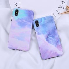 two phone cases are sitting on top of a white sheet with blue and purple clouds