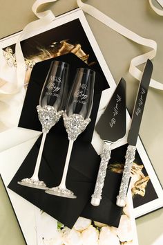 two wine glasses and a knife sitting on top of a black card with white ribbon