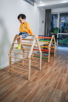 a young boy sitting on top of a wooden toy slide in a room with hard wood flooring