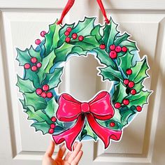 a hand holding up a christmas wreath door hanger with holly and red berries on it