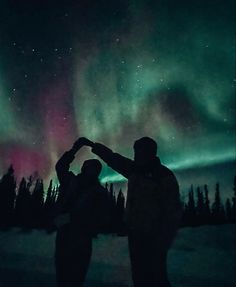 two people are standing in the snow with their arms around each other and looking at the sky